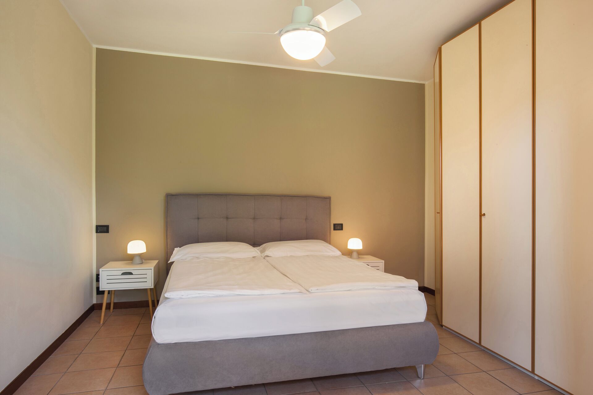 Un dormitorio con cama, mesitas de noche, ventilador de techo y armario.