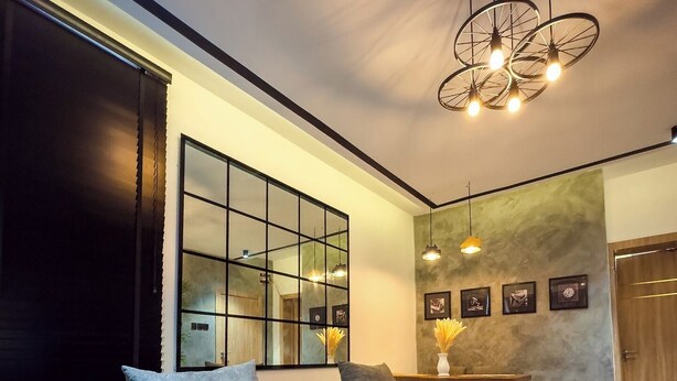 A modern living room with a sectional sofa, a coffee table, and a large mirror. There is a dining area with a table and chairs, and a chandelier hanging from the ceiling.