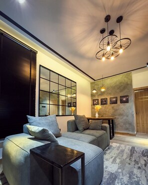 A modern living room with a sectional sofa, a coffee table, and a large mirror. There is a dining area with a table and chairs, and a chandelier hanging from the ceiling. - Crestville Apartments (Lagos)