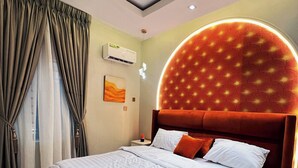 A modern hotel room with a large bed, a headboard with a circular light design, and a ceiling with recessed lighting.