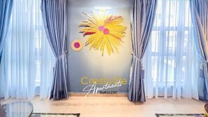 A room with a large window, grey curtains, a wall-mounted artwork, and a sign reading "Crescent Apartments".