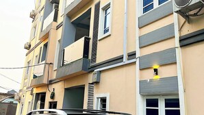 A multi-story residential building with balconies, air conditioning units, and a car parked in front.