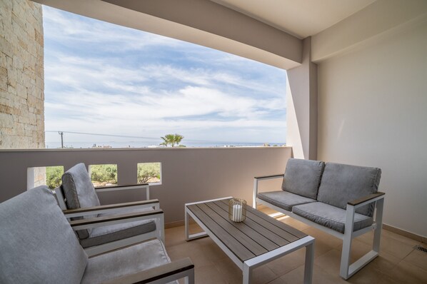 A balcony with a grey sofa, a wooden table, and a view of the sea. - Villa Zoe - With 72m Pool (Ierapetra)