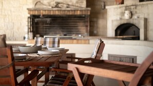 A rustic dining area with a stone fireplace, wooden furniture, and a stone wall. - Villa Zoe - With 72m Pool (Ierapetra)