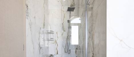 Un baño moderno con paredes de mármol, cabina de ducha con vidrio y ducha visible.