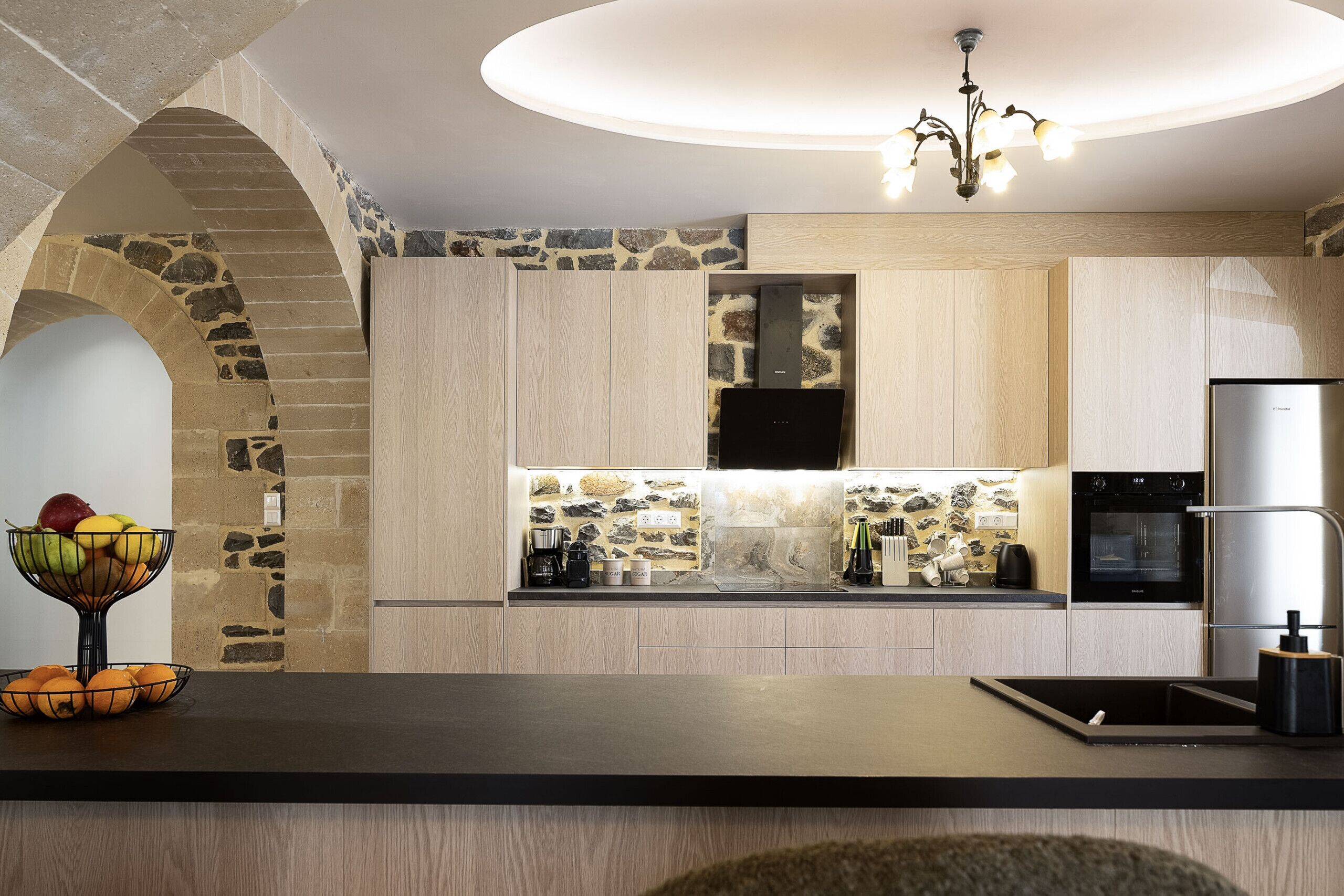 Una cocina moderna con un arco de piedra, armarios de madera, horno empotrado y refrigerador de acero inoxidable.
