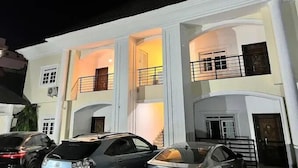 A multi-story building with a white facade, multiple balconies, and a parking area with several cars. - Blue Velvet Apartments (Abuja)