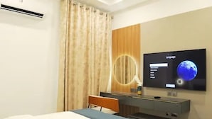 A hotel room with a bed, a desk with a computer, a TV on the wall, and a large window with curtains. - Blue Velvet Apartments (Abuja)