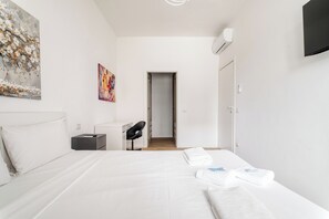 Una habitación de hotel moderna con una cama grande, un escritorio, una silla y un televisor montado en la pared.