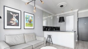 A modern kitchen with a white countertop, a black hanging light fixture, and a stainless steel refrigerator. - RentPlanet - Apartament Siedmiogrodzka (Warsaw)