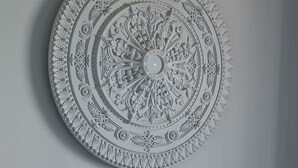 A circular wall decoration with intricate patterns, a plain wall, and a white headboard with pillows. - RentPlanet - Apartament Siedmiogrodzka (Warsaw)