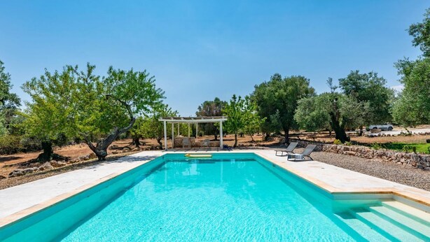 A rectangular swimming pool with a pergola and lounge chairs in a landscaped area with trees. - Casa di Paolo - Lamia by Rentbeat (Ceglie Messapica)