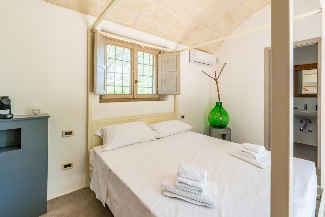 A hotel room with a bed, a window, a green vase, and a desk with a coffee maker.