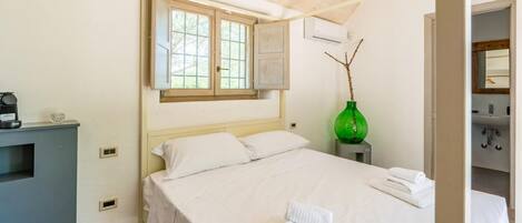 A hotel room with a bed, a window, a green vase, and a desk with a coffee maker.