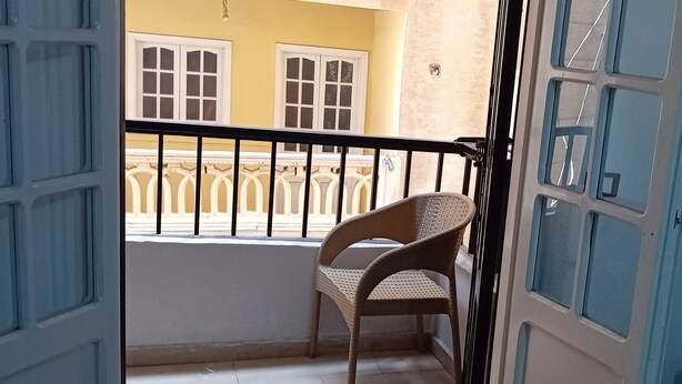 A balcony with a wicker chair, a railing, and a view of a yellow building with white windows. - Furnished apartment for rent in miamiAlexandria (Alexandria Governorate)