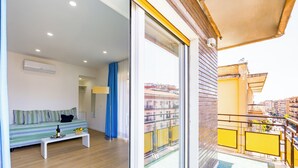 A balcony with a view of buildings, a sofa, a bench, and a table with a bottle and glasses. - Carlo III guest house (Naples)