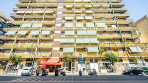 A multi-story building with balconies, a street in front, and a few parked vehicles. - Carlo III guest house (Naples)