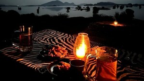 A table set for a meal with a zebra-patterned tablecloth, a candle, and glasses of a reddish beverage.