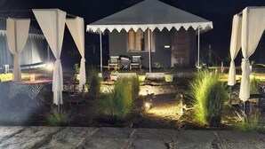 A tented outdoor area with stone flooring, two chairs, and potted plants.