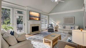 A spacious living room with a fireplace, a large TV mounted above it, and a comfortable seating area with a sofa and armchairs.