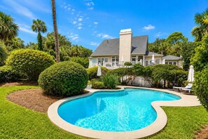 A swimming pool with a curved edge, surrounded by well-maintained grass and various shrubs.