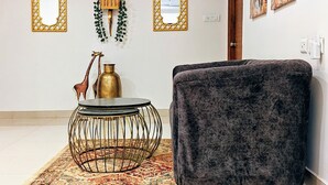 A room with a dark velvet sofa, a round metal-framed table, a patterned rug, and decorative wall art.