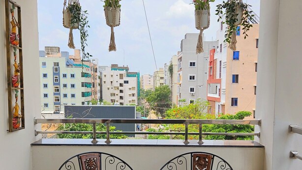 A balcony with a table and chairs, a view of buildings, and hanging planters.