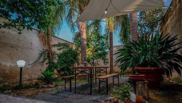 Une terrasse extérieure avec des tables et des bancs en bois, entourée de plantes en pot et d’un mur de pierre.