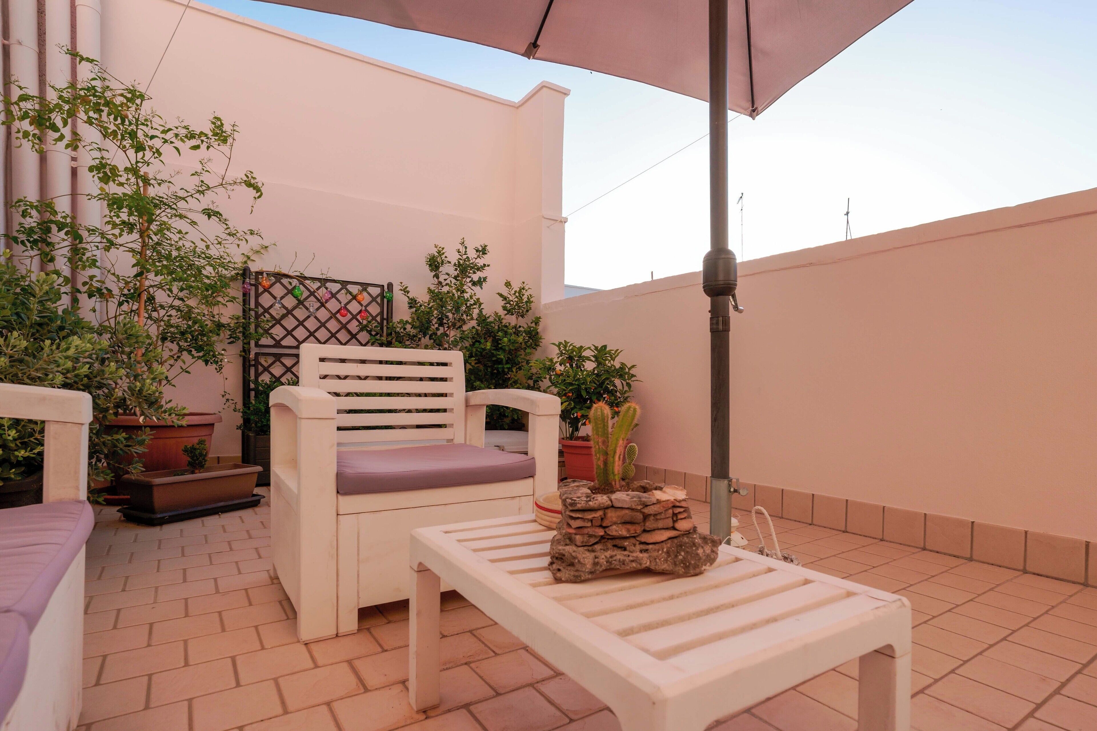 A patio with a white chair, a small table, and potted plants.
