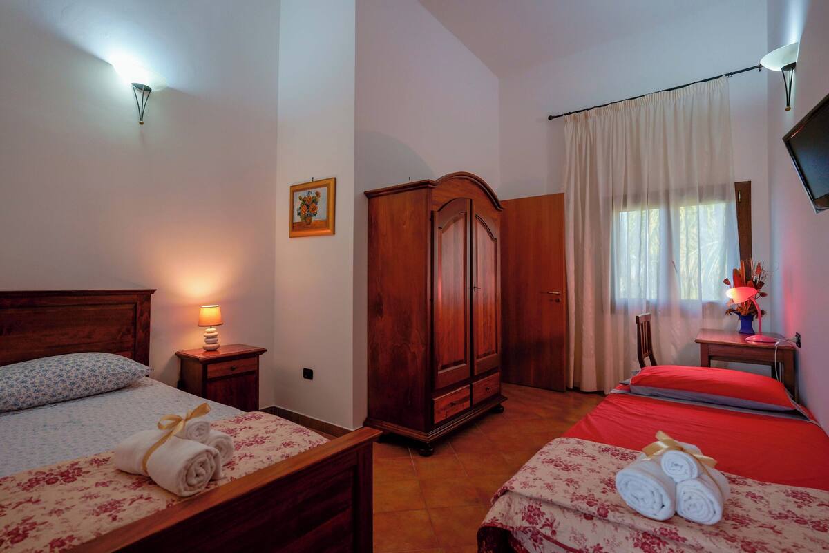 Una habitación de hotel con dos camas, un armario, un televisor y una ventana con cortinas.