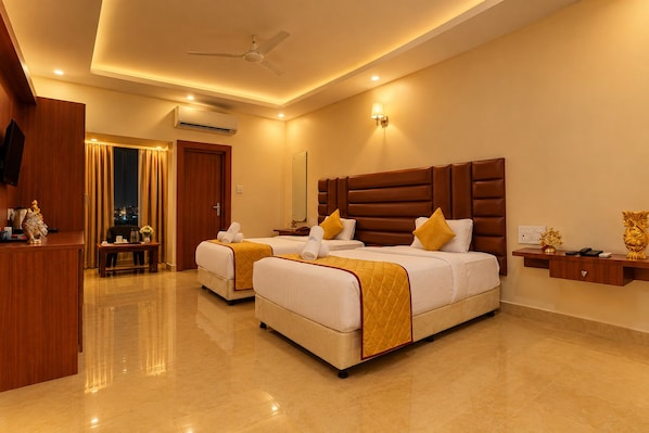 A hotel room with two beds, a desk, a chair, a TV, and a ceiling fan.