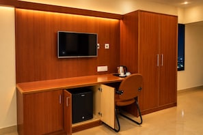 A compact hotel room with a wooden desk, a television, a minibar, and a wardrobe.