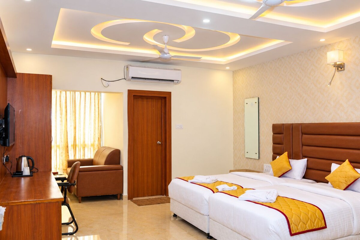 A hotel room with a large bed, a desk with a chair, a television, and an air conditioning unit.