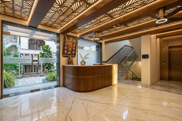 A reception area with a wooden reception desk, a ceiling with a geometric pattern, and a staircase in the background. - Hotel Lorven (Tirupati)