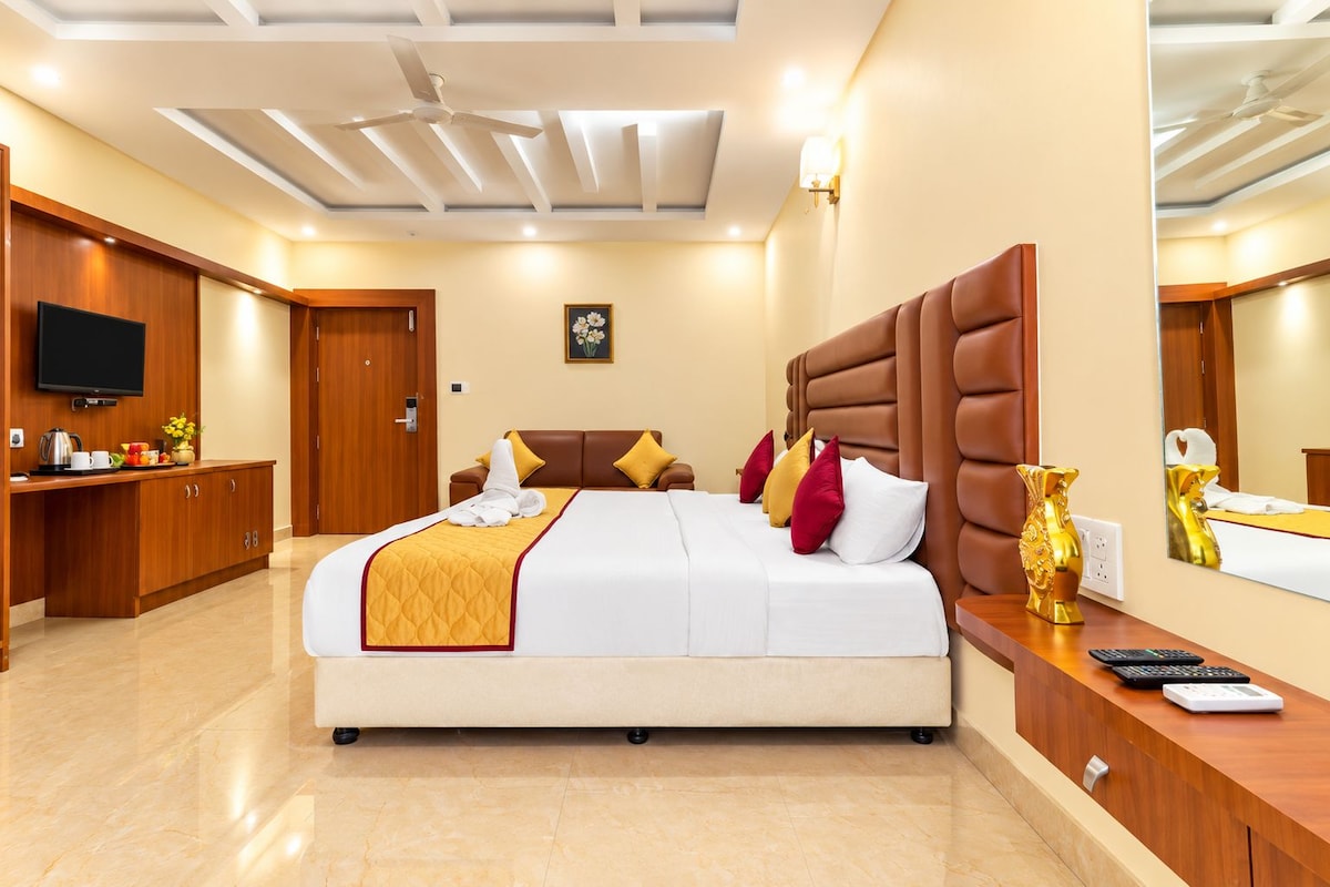 A hotel room with a large bed, a wooden desk, a television, and a bathroom visible in the background.