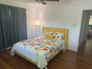 A bedroom with a bed, a ceiling fan, a bedside lamp, and a door leading to another room.