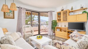 Ein Wohnzimmer mit einer Couch, einem Couchtisch, einem Fernseher und einem Balkon mit Blick.