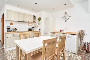 A kitchen with white cabinets, a wooden table, and chairs, a dishwasher, and a wall clock. - Apartment 'Lily' with Sea View, Wi-Fi and Air Conditioning (Almuñécar)