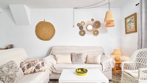 Ein Wohnzimmer mit einer Couch, einem weißen Couchtisch, Korbstühlen, einer Wand mit Dekoration und einer Lampe.