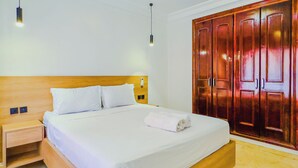 A neatly made bed with white linens, a wooden headboard, and a wooden wardrobe with two doors.