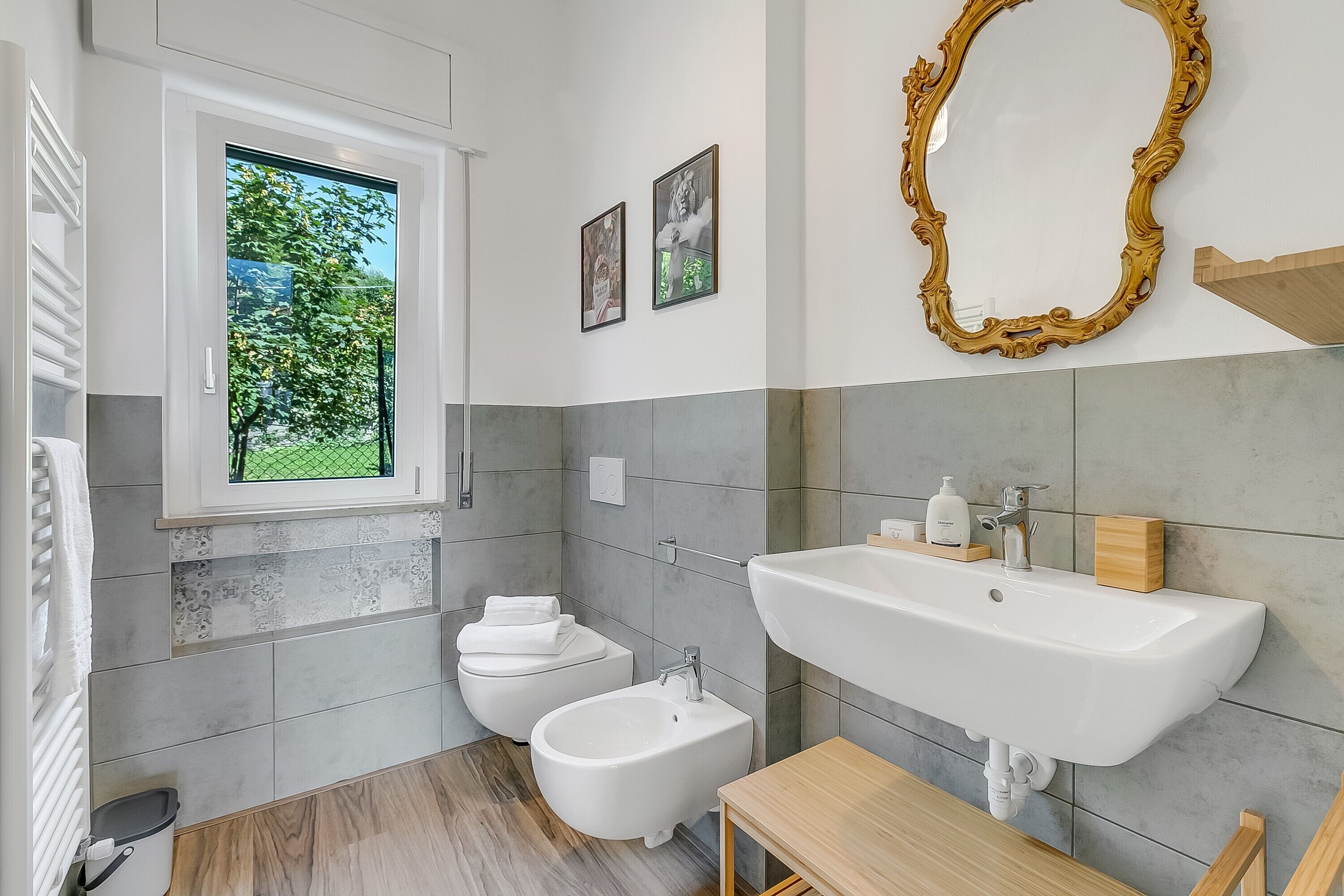 A modern bathroom with a large sink, a bidet, and a window with a view of greenery.
