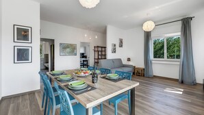 A modern dining area with a wooden table, blue chairs, and a view of a kitchen and living room. - Casa Tramonti: Mountain-view With Terrace Dining (Gemonio)