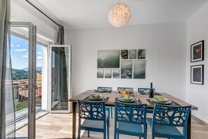 A dining area with a table set for four, blue chairs, and a view of the outdoors through a sliding door. - Casa Tramonti: Mountain-view With Terrace Dining (Gemonio)