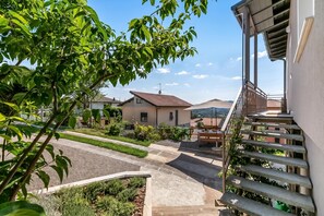 Una zona residenziale con vialetto lastricato, una scala che conduce a un balcone e vista sulle case vicine.