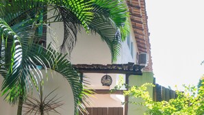 Entrada fechada com palmeira e um vaso, número 12 na parede, e um banco na parte externa.
