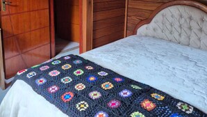 Ein Schlafzimmer mit Holztür, einem Bett mit weißer Bettdecke und einer bunten Häkeldecke.