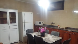 A compact kitchen with a refrigerator, microwave, and a dining table with chairs. - Lovely Appartment in Daroun. Kesserwan (kesrwan)