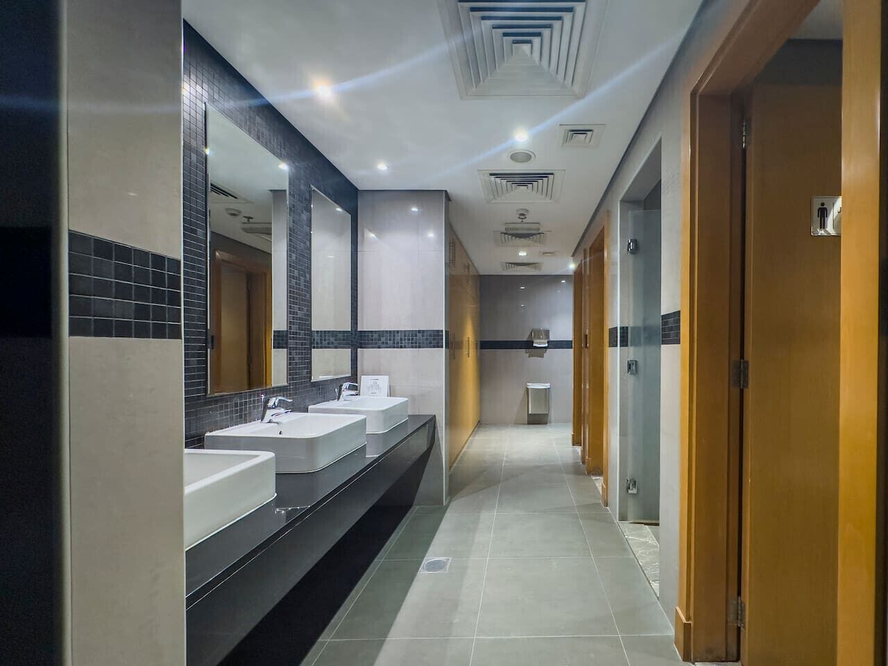 A modern bathroom with three sinks, a large mirror, and a tiled floor.