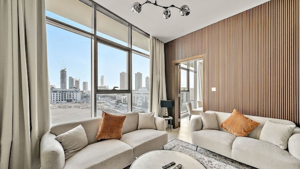 Ein modernes Hotelzimmer mit großem Fenster und Blick auf die Stadt, einer Sofagruppe, einem kleinen Tisch und einer Lampe.