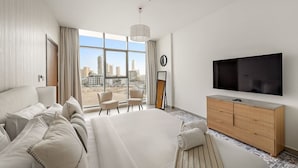 Ein modernes Hotelzimmer mit einem großen Bett, einem Fernseher, einer hölzernen Kommode und Blick auf die Stadt durch die Fenster.
